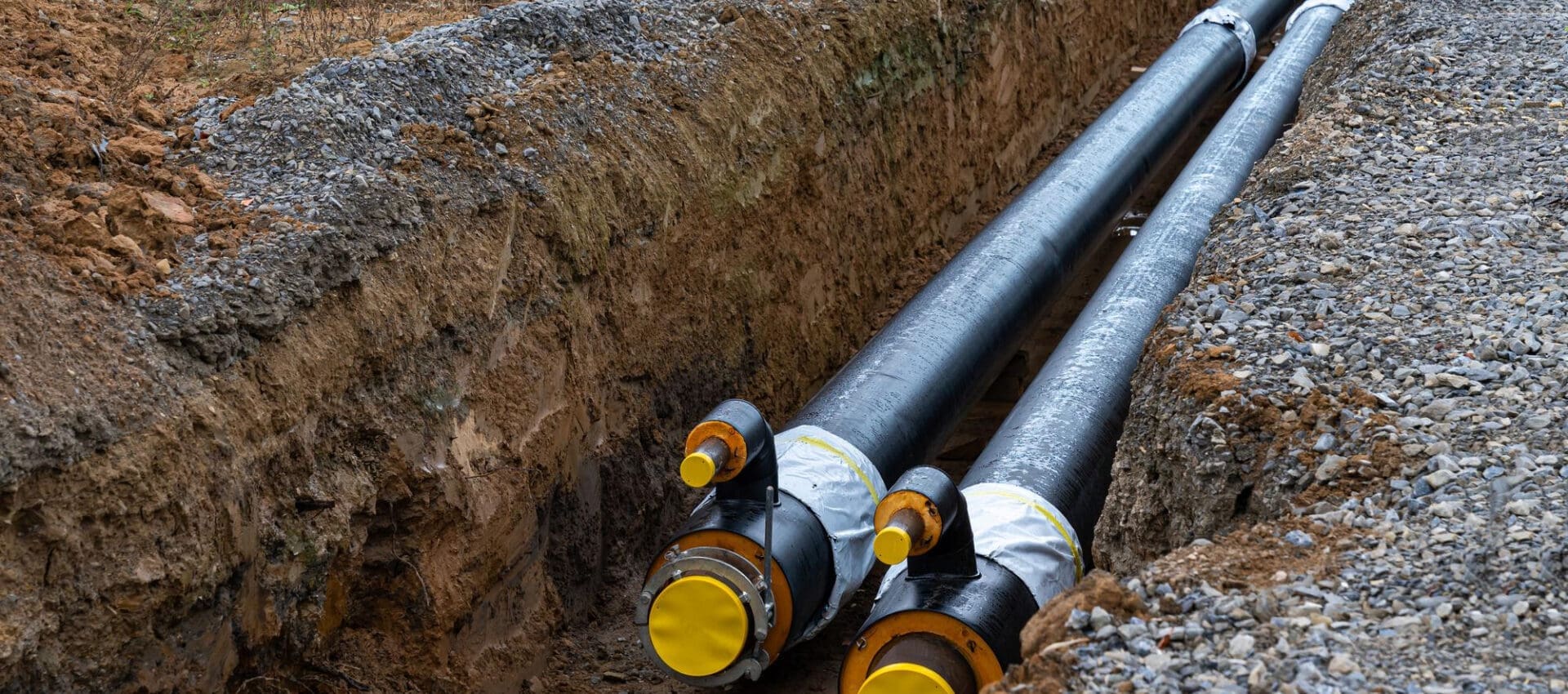 Large black gas pipes with a plastic sheath are installed in trenches as part of a modern pipeline system